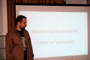 Prelegent dr Bartłomiej Chromik na tle prezentacji z widocznym slajdem na któym widnieje napis "Kęczanin na Huculszczyźnie" w języku polskim i ukraińskim.